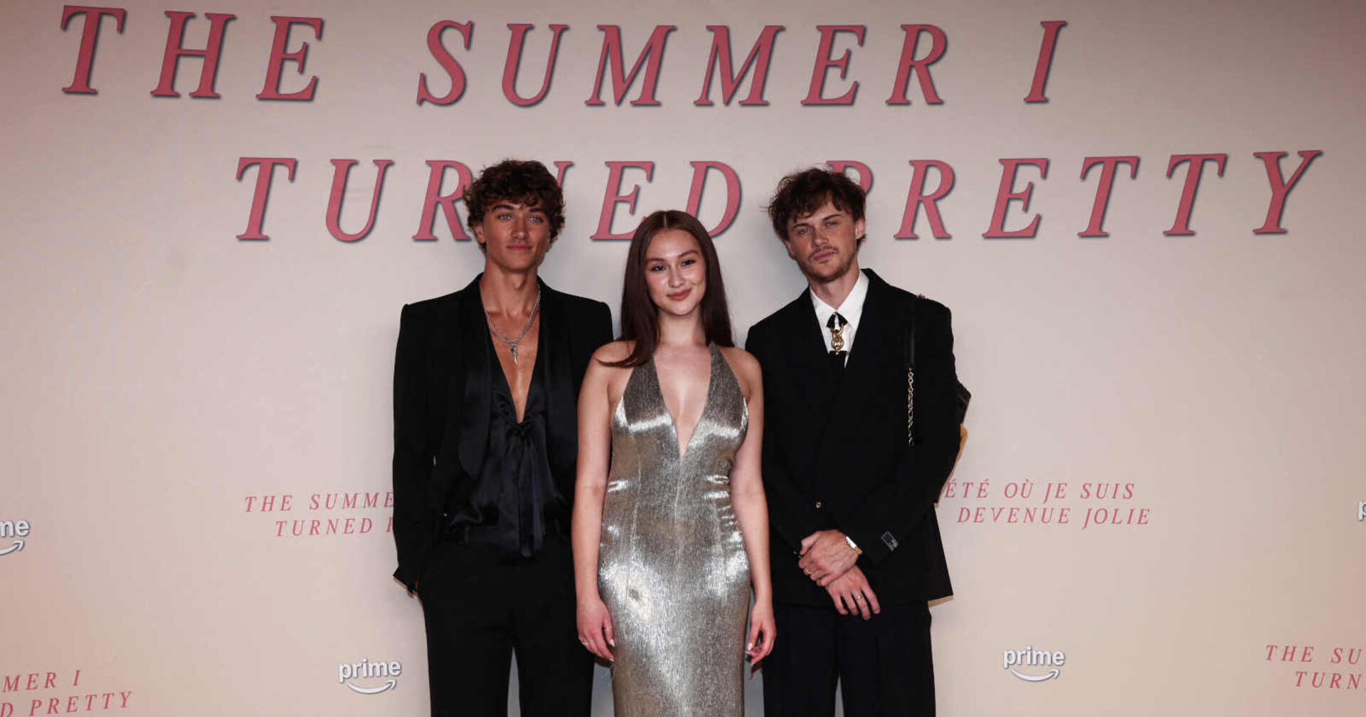 Eine Frau in einem silbernen Kleid steht zwischen zwei Männern in Anzügen