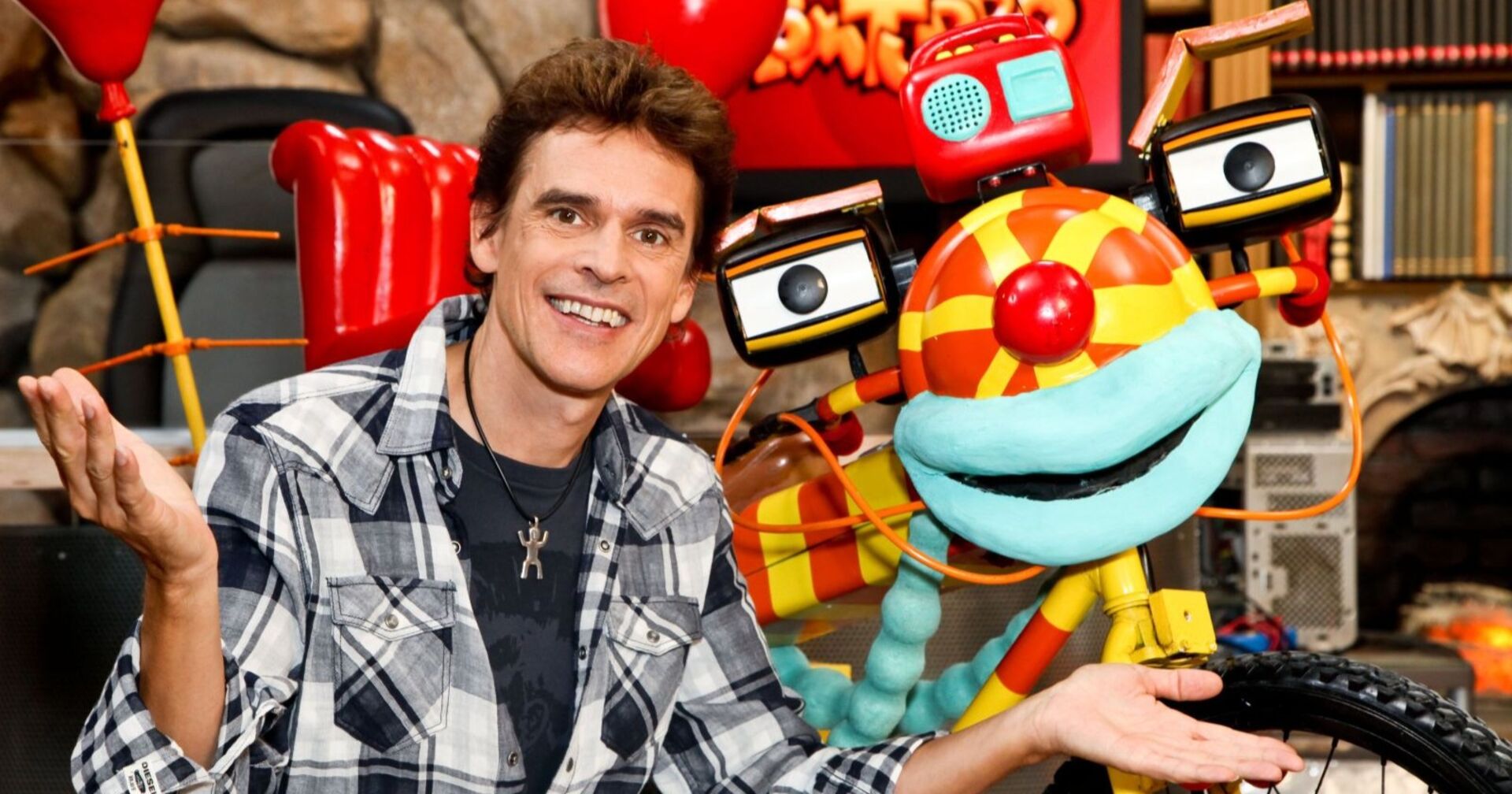 Thomas Brezina sitzt neben dem bunten Fahrrad „Tom Turbo“ und lächelt in die Kamera.