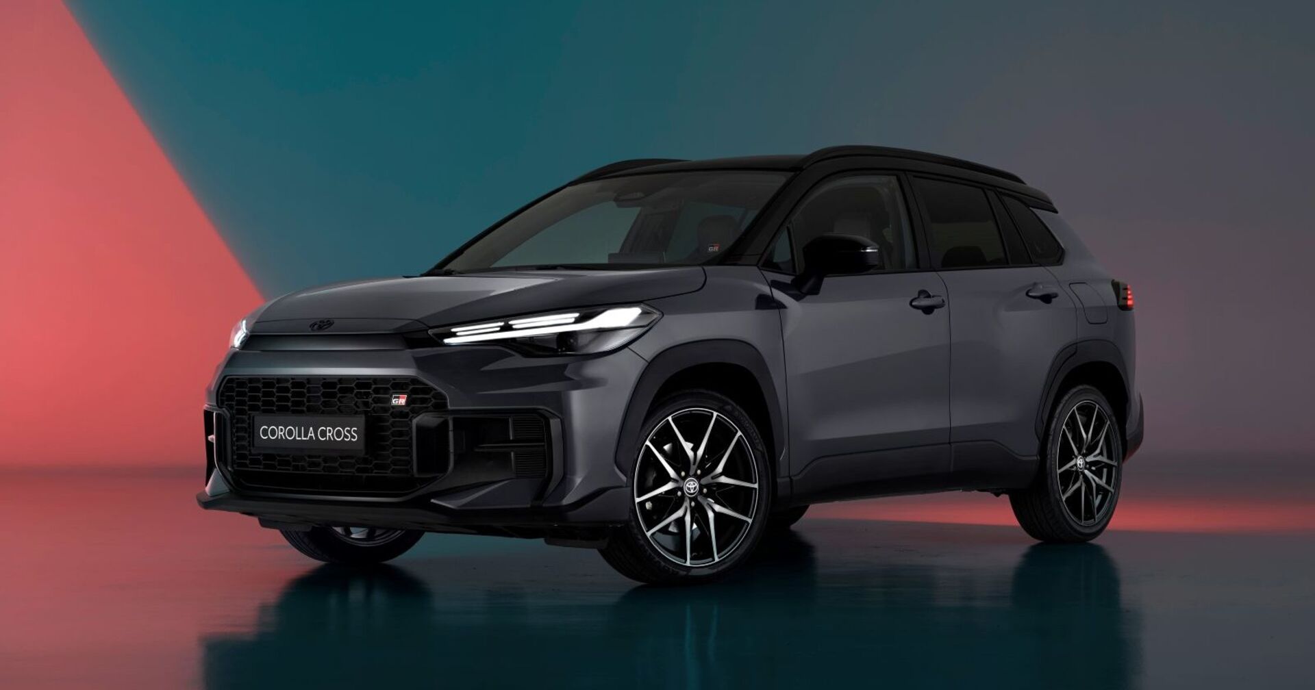 Ein schwarzer Toyota Corolla Cross parkt in einem Schauraum. Der Raum erstrahlt in blauen und roten Farbtönen.