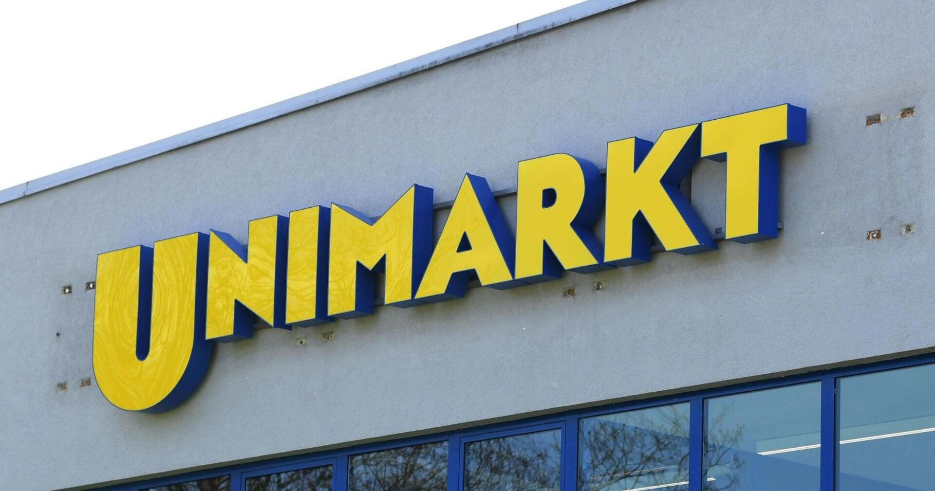 Gelbes Unimarkt-Logo auf grauer Fassade eines Supermarkts, Symbol für die angekündigte Schließung aller Filialen.