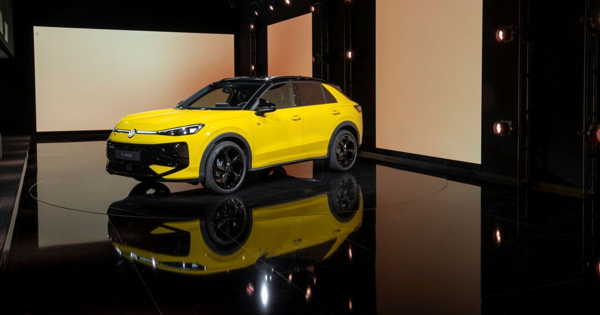 Ein gelber VW T-Rock steht in einem Raum, der mit einem spiegelnden, schwarzen Boden ausgestattet ist.