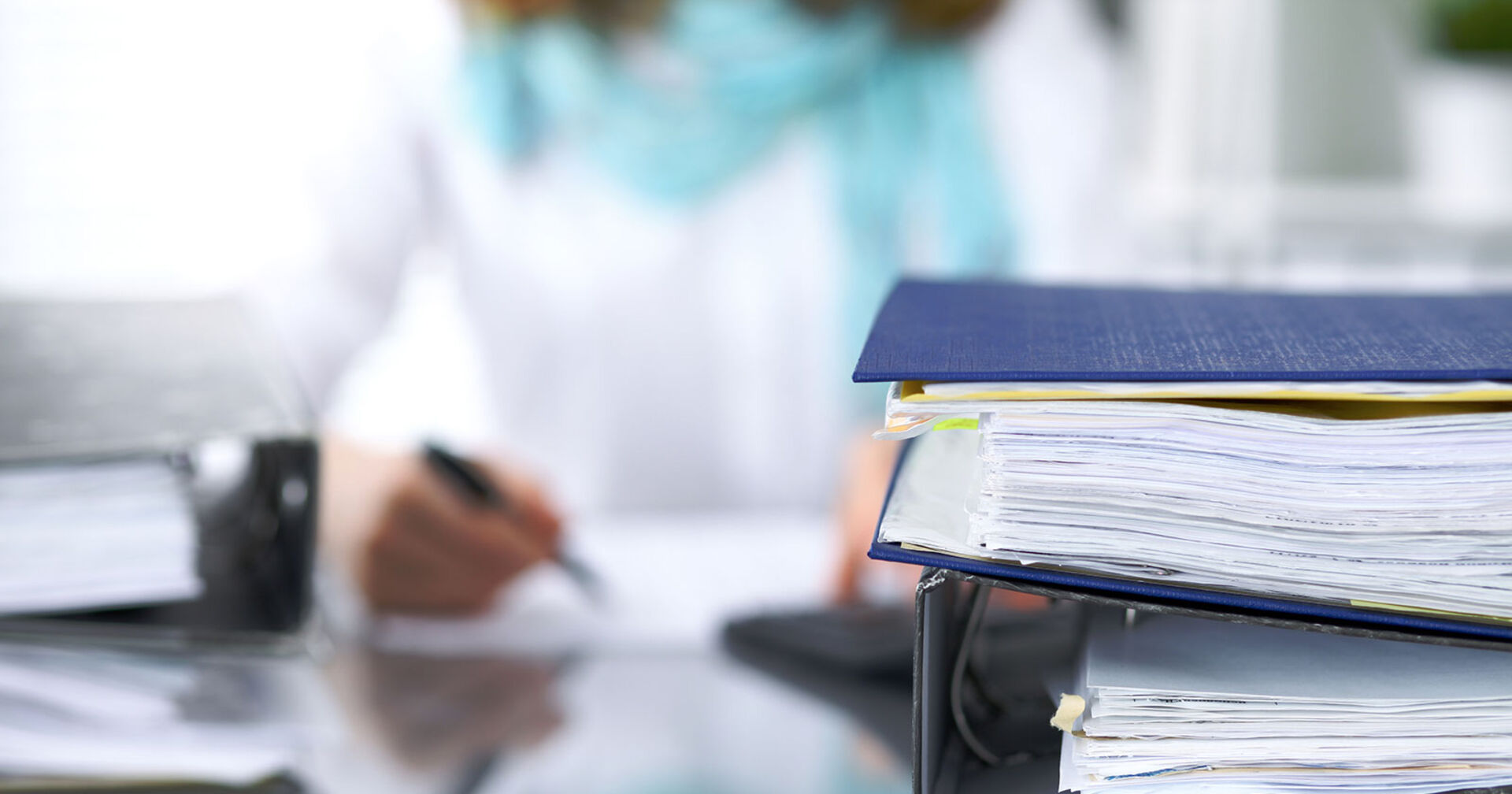 Frau hinter Aktenmappen bei der Arbeit | Credit: iStock.com/andrei_r
