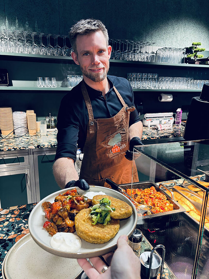 Männliche Bedienung in einem Lokal gibt ein Essen aus | Credit: Hilfswerk Salzburg/das Urstein