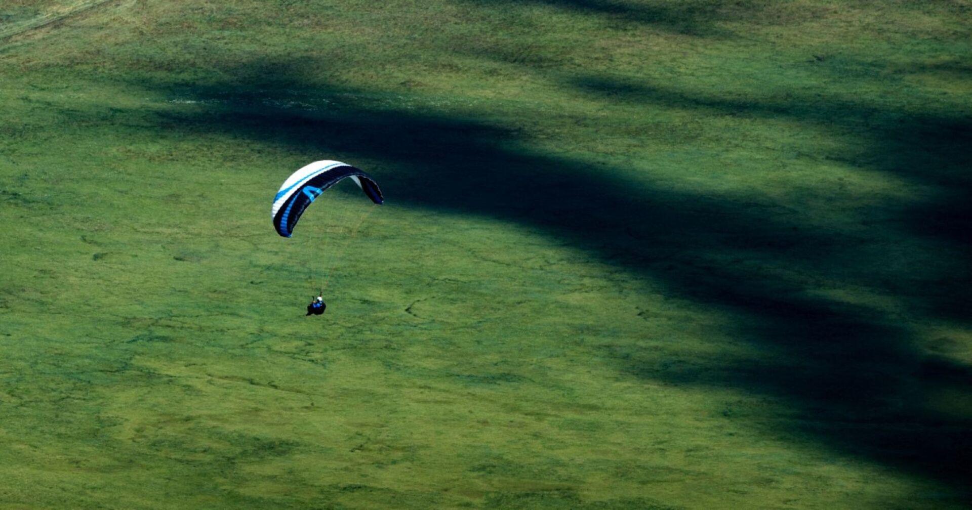 Drachenflieger mit Schirm in der Luft über grüner Wiesenlandschaft am Monte Cucco in Italien.