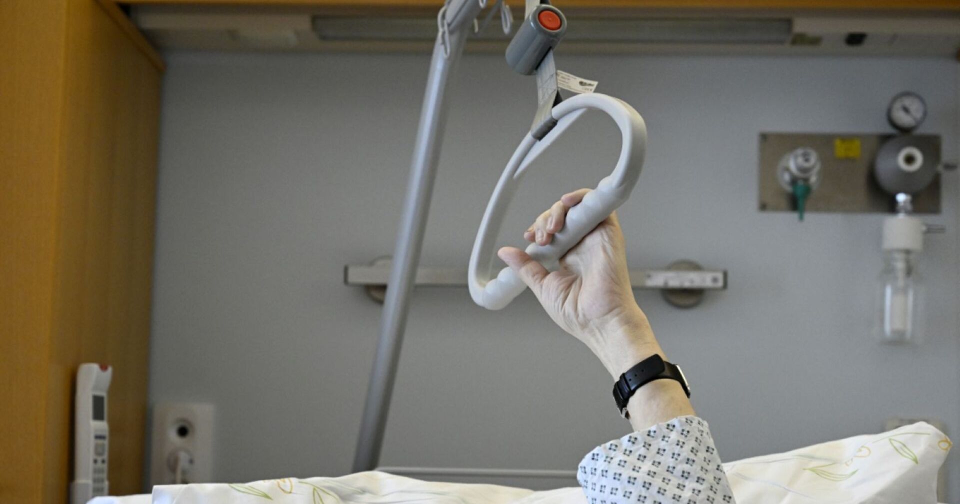 Mann im Krankenbett, der sich an einem Griff festhält