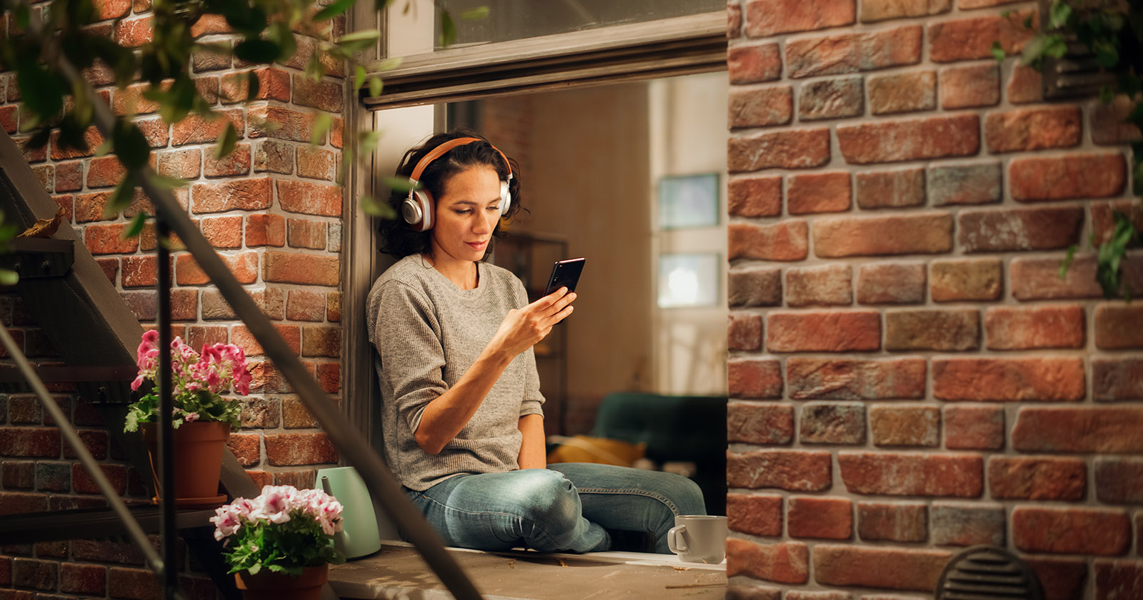 Frau sitzt am Fenster und hört einen Podcast | Credit: iStock.com/gorodenkoff