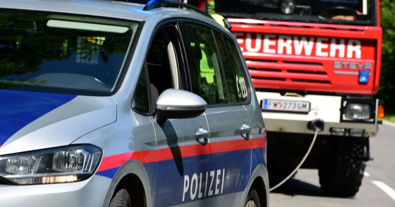 Ein Polizeiwagen und ein Feuerwehrfahrzeug stehen im Einsatz auf einer Wiener Straße nach einem Autobrand.