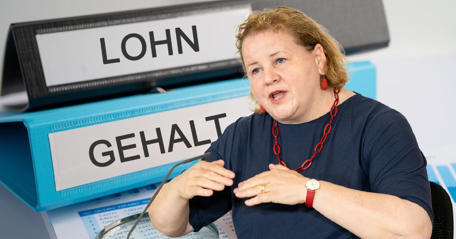 Korinna Schumann spricht über das Lohntransparenz-Gesetz, im Hintergrund Aktenordner mit der Aufschrift „Lohn“ und „Gehalt“.