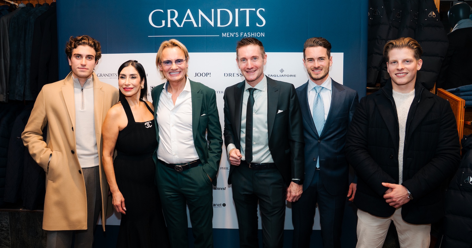 Sechs Männer und eine Dame vor einer türkisen Wand im  Grandits Men's Fashion-Store