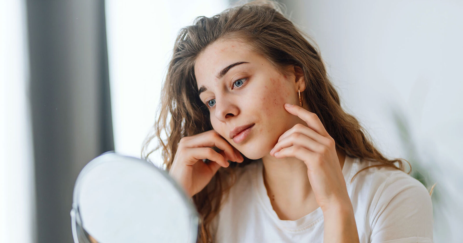 Frau schaut sich ihre Haut im Spiegel an | Credit: iStock.com/Maksym Belchenko
