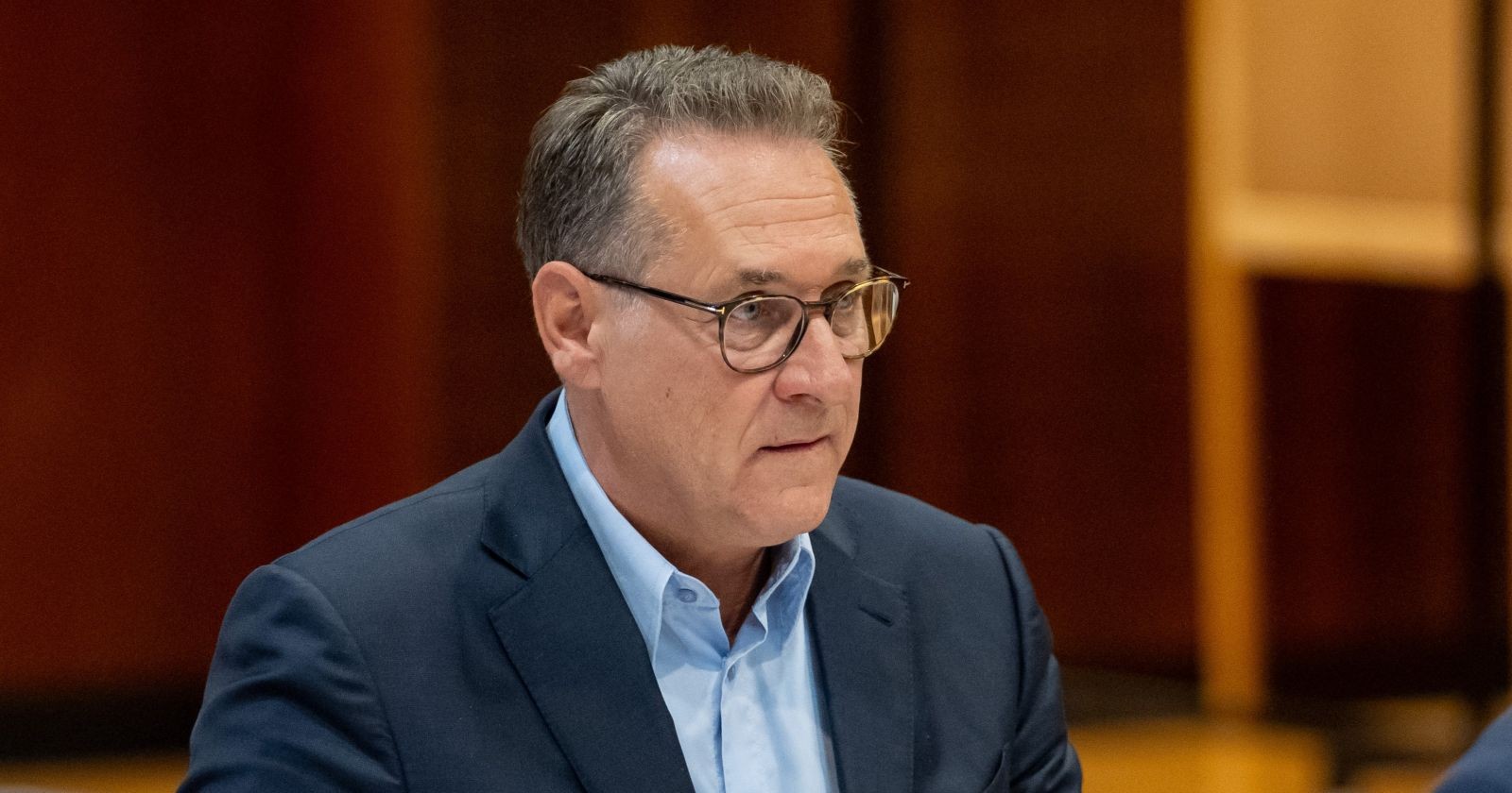 Heinz-Christian Strache sitzt in einem Sitzungsraum und trägt Anzug und Brille.