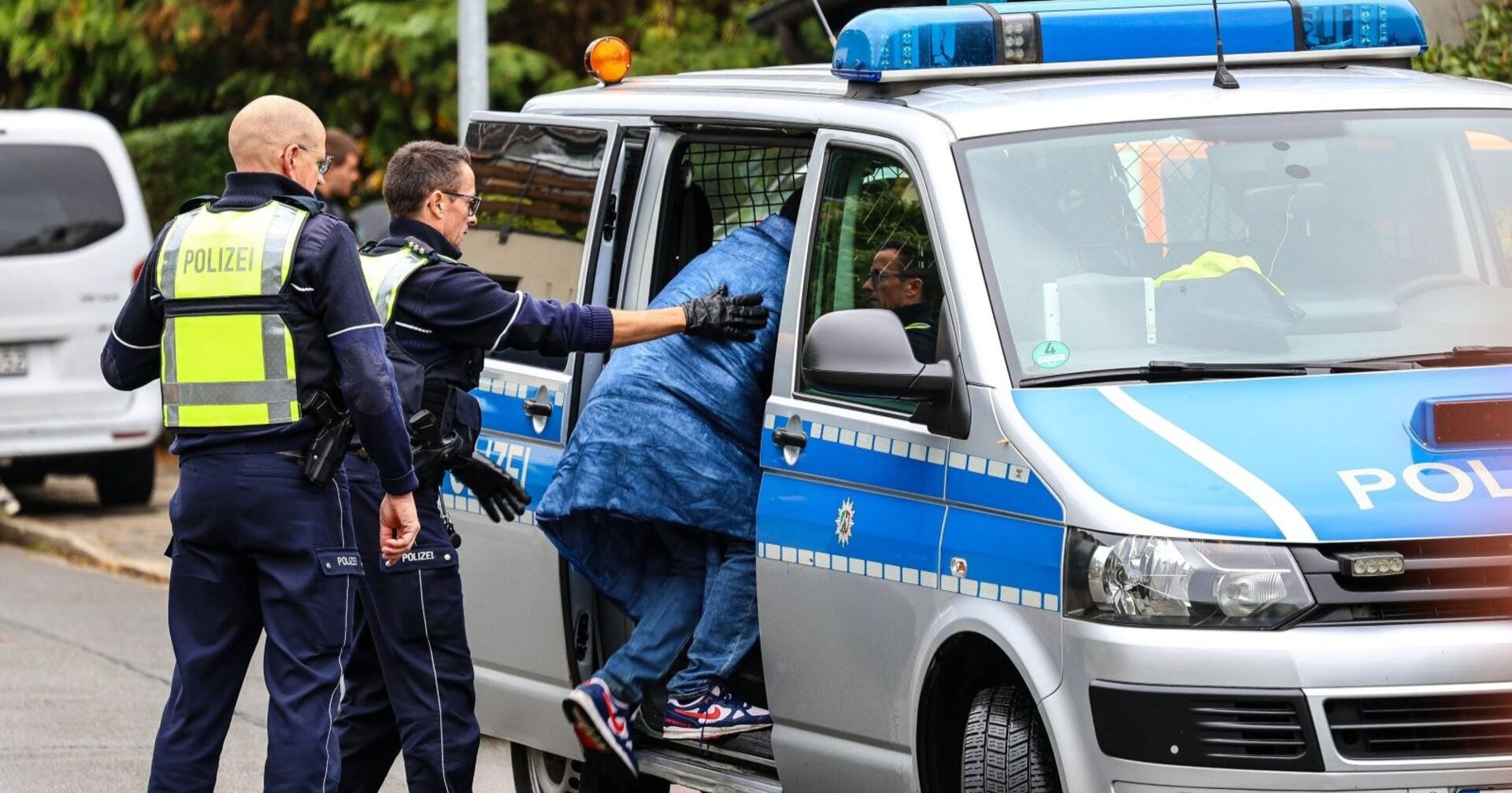 Mehrere Polizisten führen eine Person zu einem Streifenwagen und sichern den Transport im Rahmen der Ermittlungen in Herdecke.
