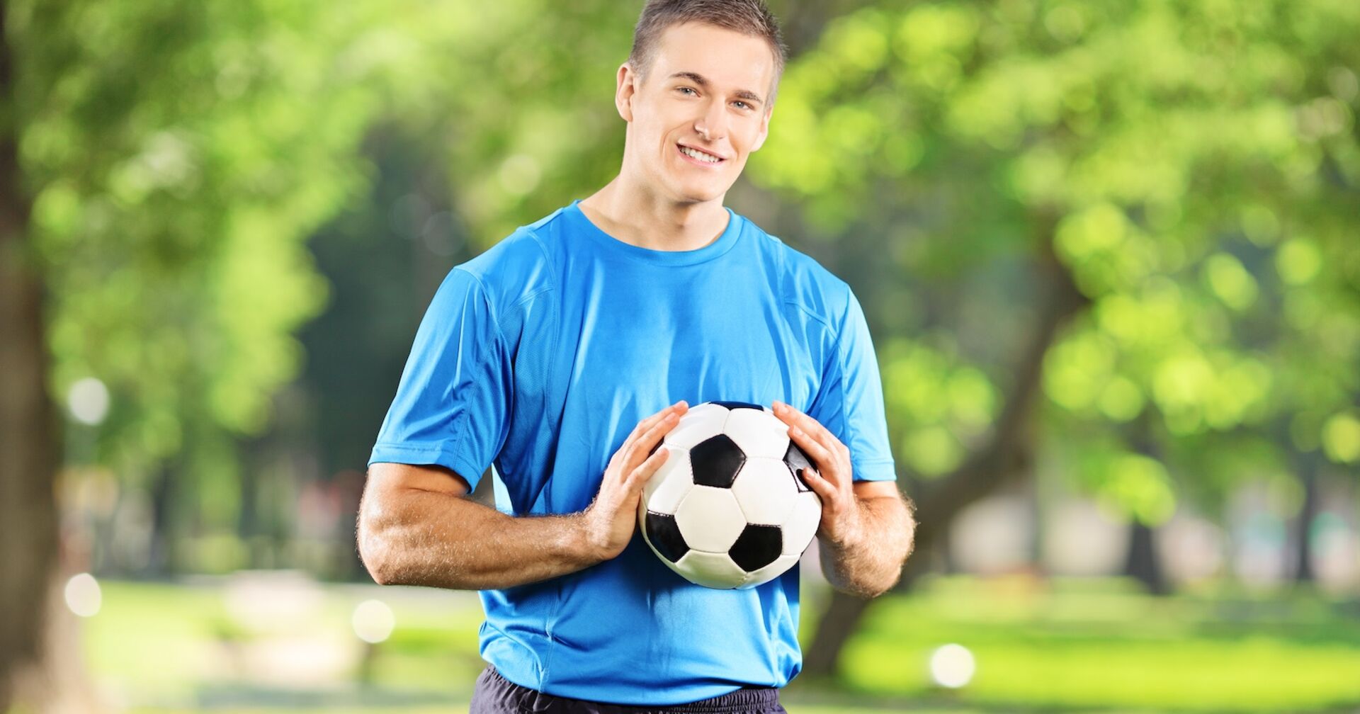 Hobbyfussballer im blauen Trikot hält einen Ball in seinen Händen