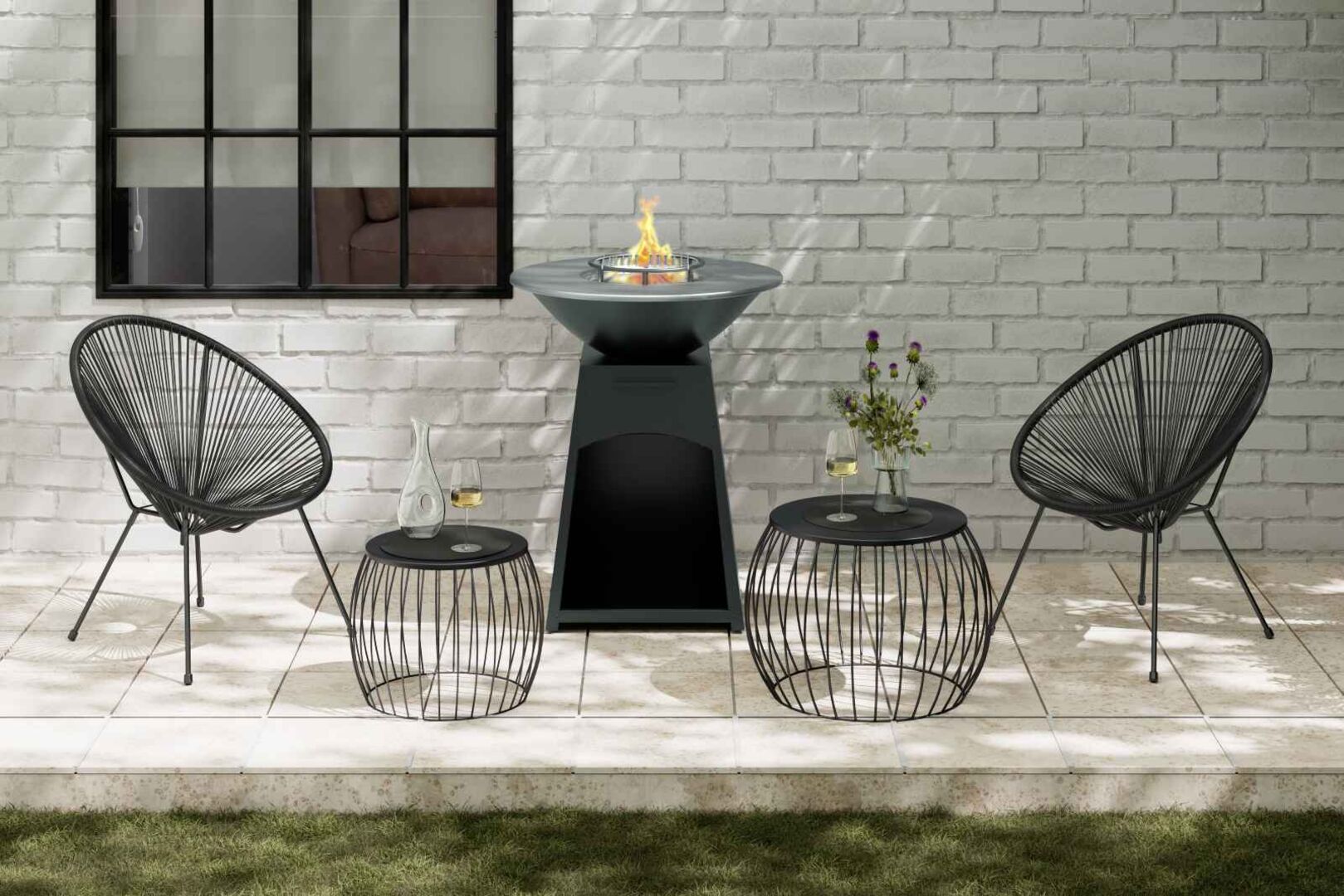 Moderne Terrasse mit stilvollen schwarzen Gartenstühlen, zwei Beistelltischen mit Gläsern und Vase sowie zentraler Feuerschale oder Holzkohlegrill auf hellem Steinboden.