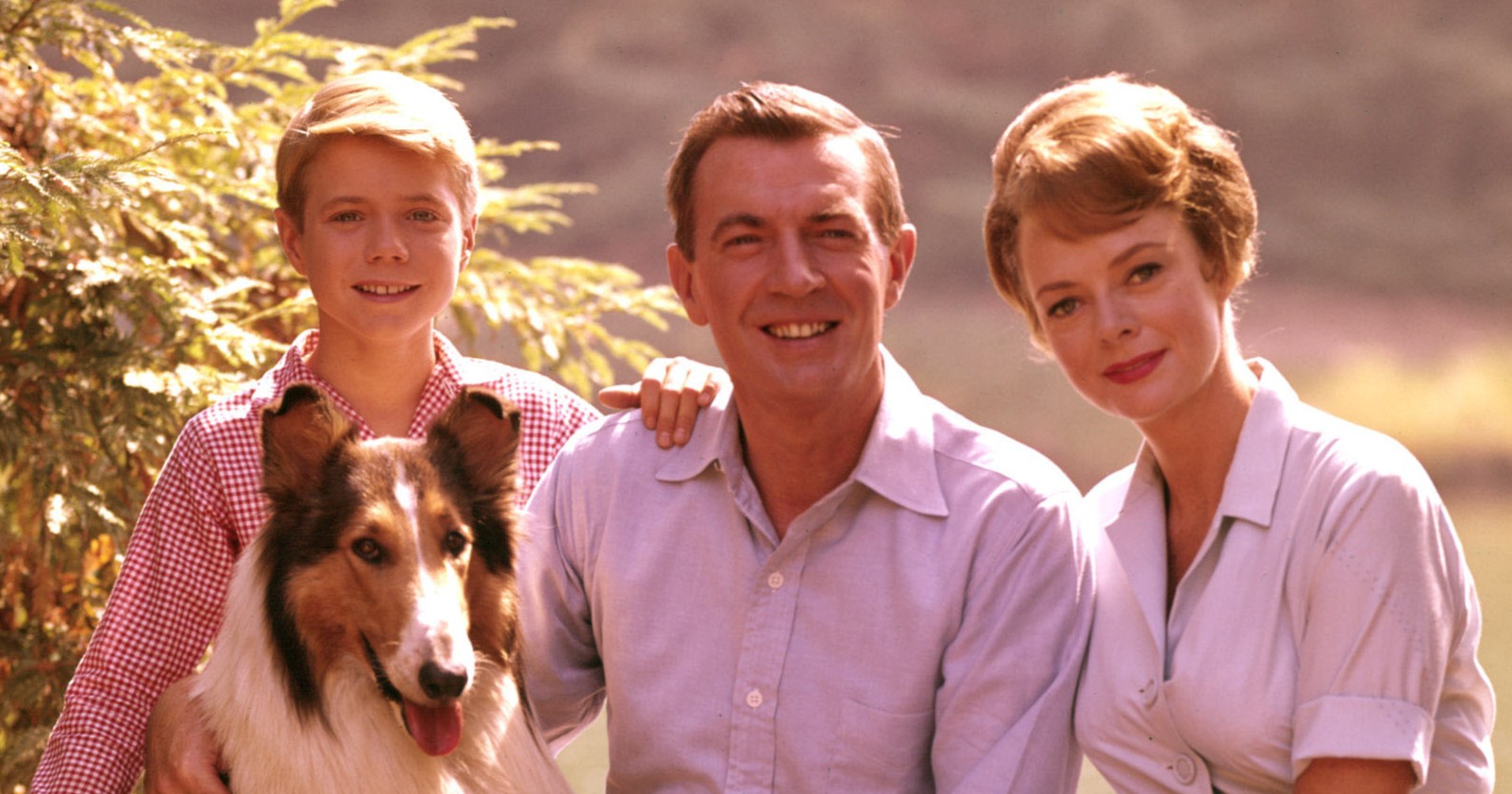 Die Martin-Familie aus der Fernsehserie „Lassie“ sitzt gemeinsam mit dem Collie Lassie im Freien und lächelt in die Kamera.