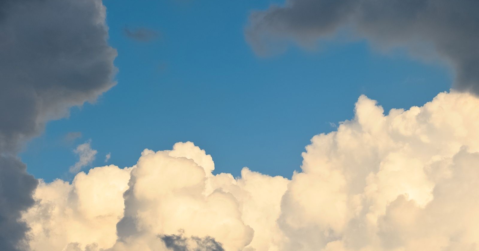Dunkle Wolken und weiße Quellwolken vor einem blauen Himmel.