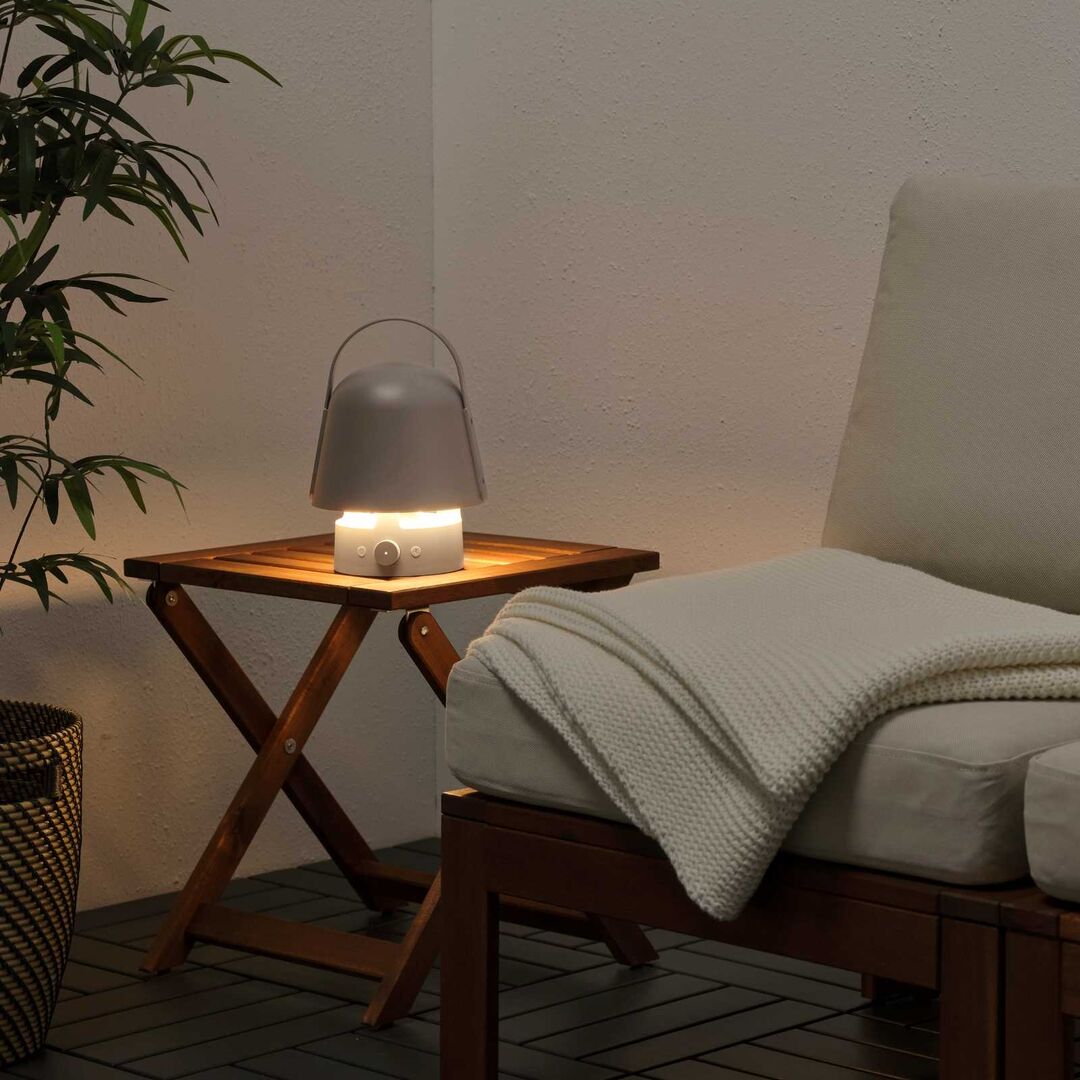 Gemütliche Sitzecke mit Holzstuhl, Decke und kleiner Tischleuchte in sanftem Licht – tragbare Lampe mit Lautsprecherfunktion sorgt für stimmungsvolle Atmosphäre.