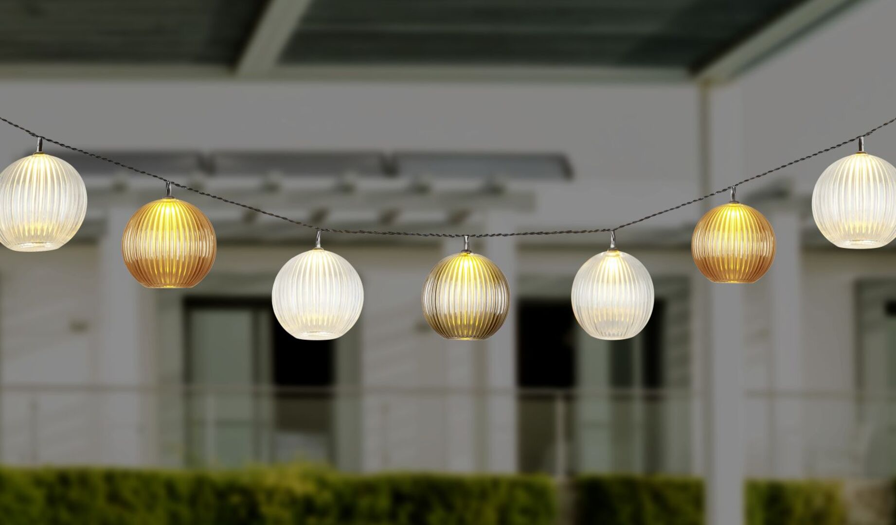 Warm leuchtende Kugel-Lichterkette mit goldenen und weißen Lampions, aufgehängt im Außenbereich – stimmungsvolle Beleuchtung für Garten oder Terrasse.