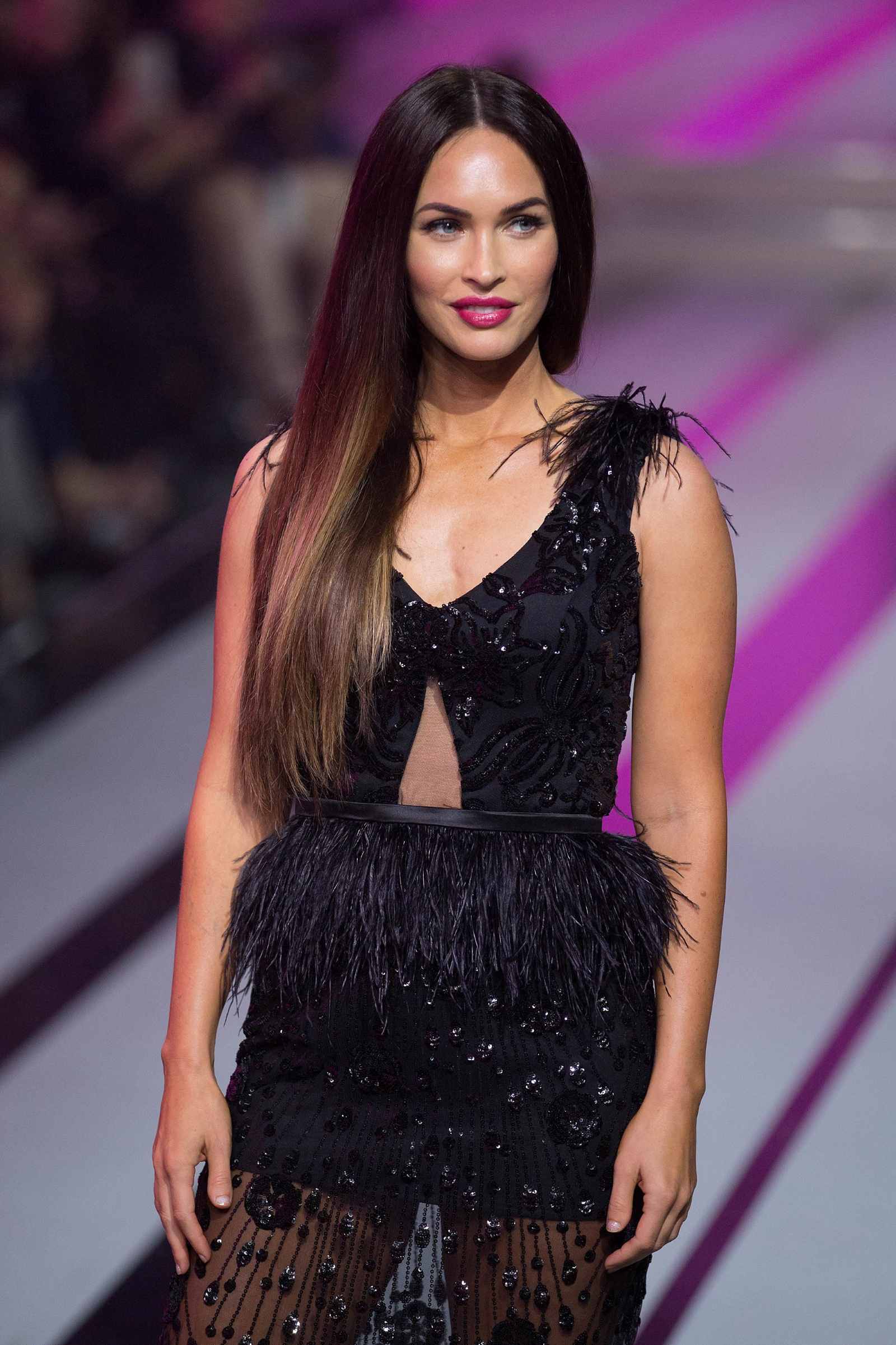 Megan Fox in einem schwarzen, funkelnden Kleid mit Federdetails.