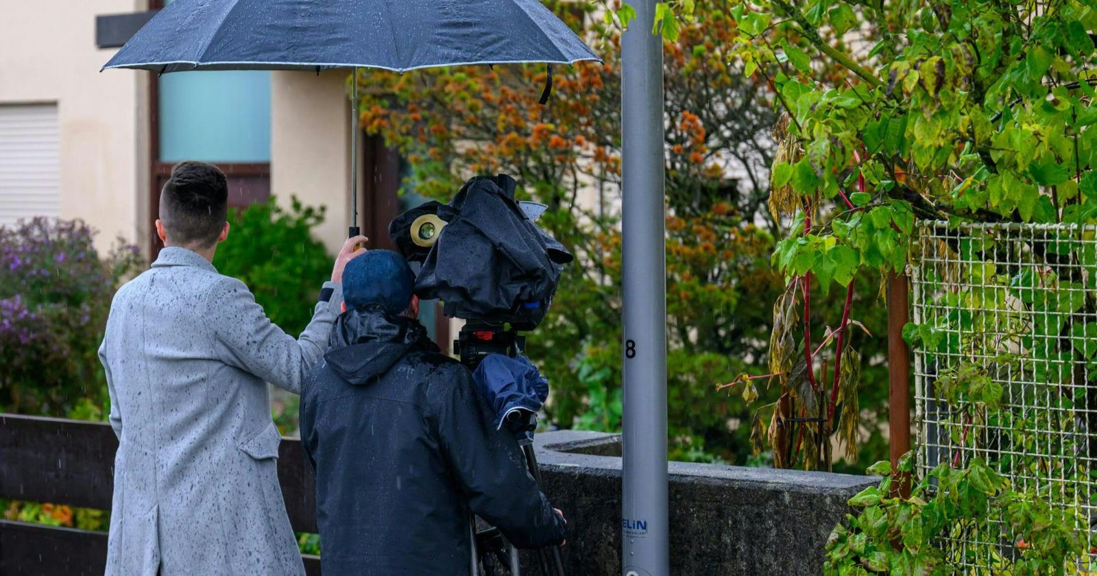 Journalistenteam mit Kamera und Regenschirm dokumentiert den Tatort in Enns nach dem mutmaßlichen Doppelmord.