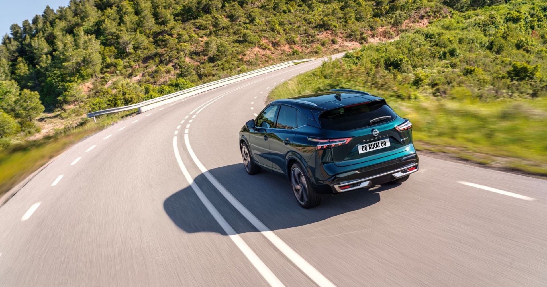 Ein grüner Nissan Qashqai fährt auf ein einsamen Landstraße. Links und rechts wachsen niedrige Bäume und Büsche, die an eine Landschaft in Südeuropa erinnern.