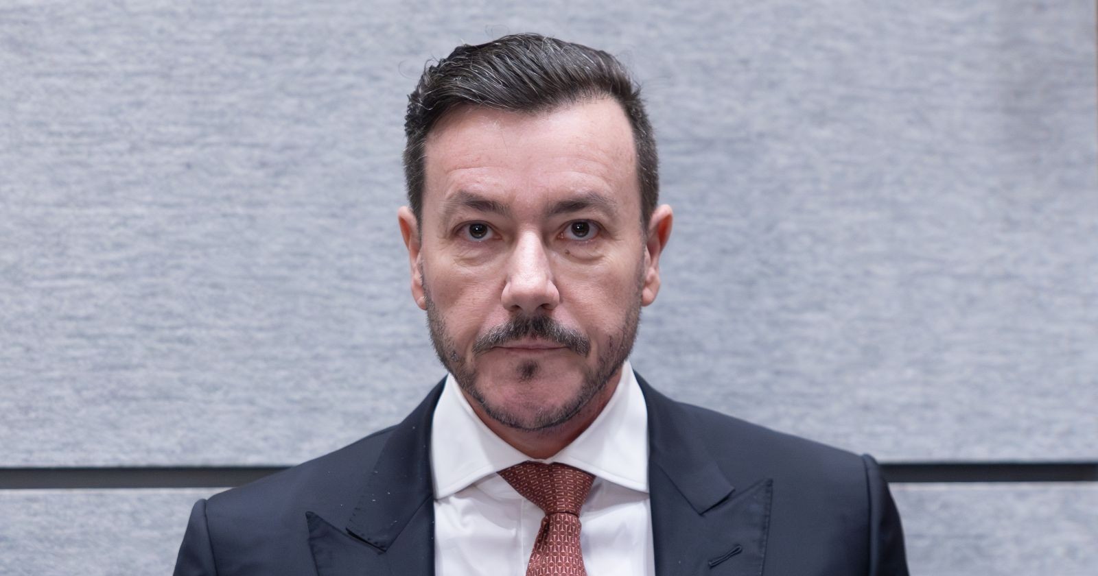 René Benko im Gerichtssaal in Innsbruck, Blick nach vorne, ernster Gesichtsausdruck, erster Prozesstag wegen Betrugsverdachts.