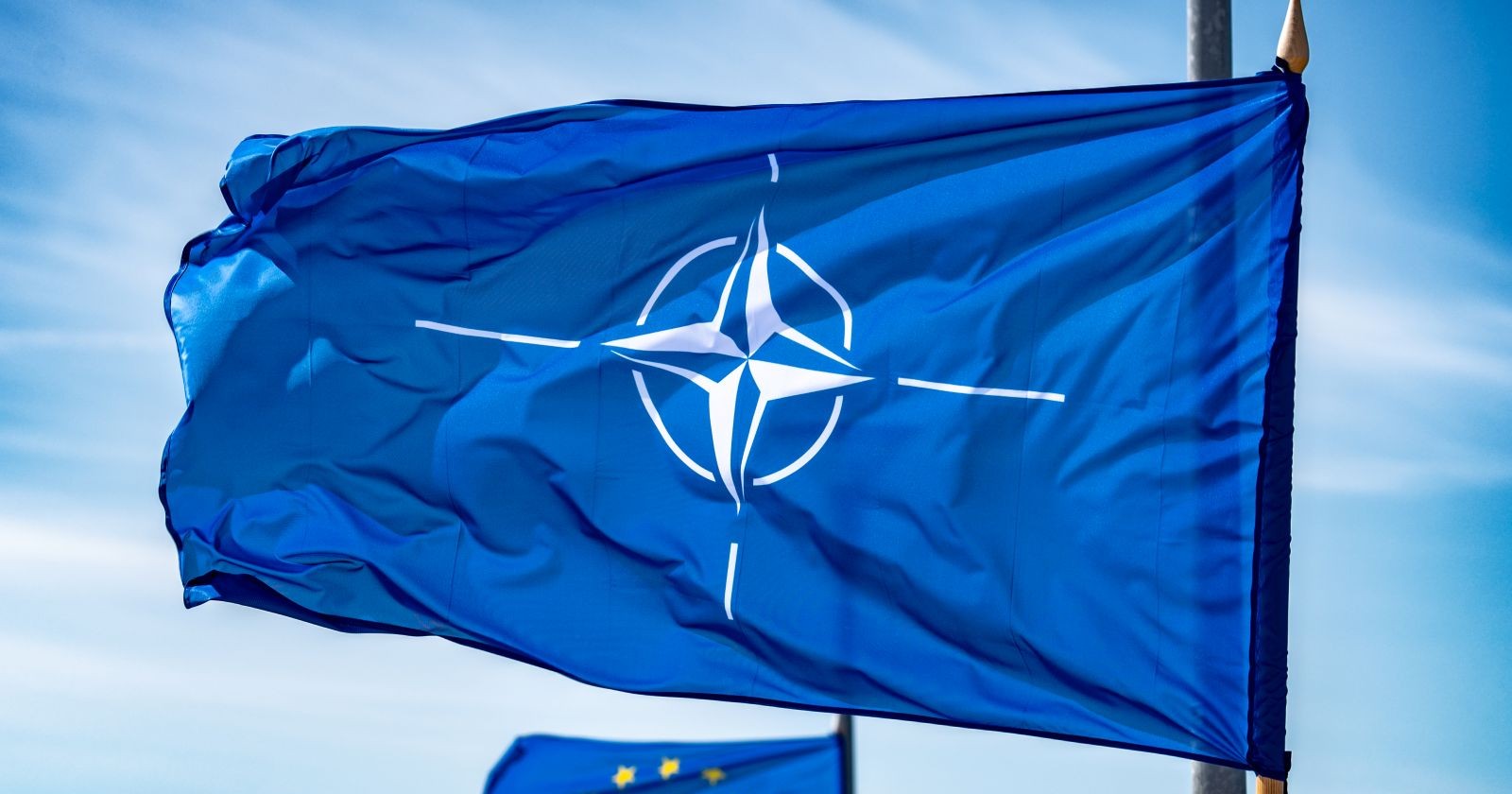 NATO-Flagge schwenkt an einem Fahnenmast im Hintergrund weht eine Flagge der Europäischen Union