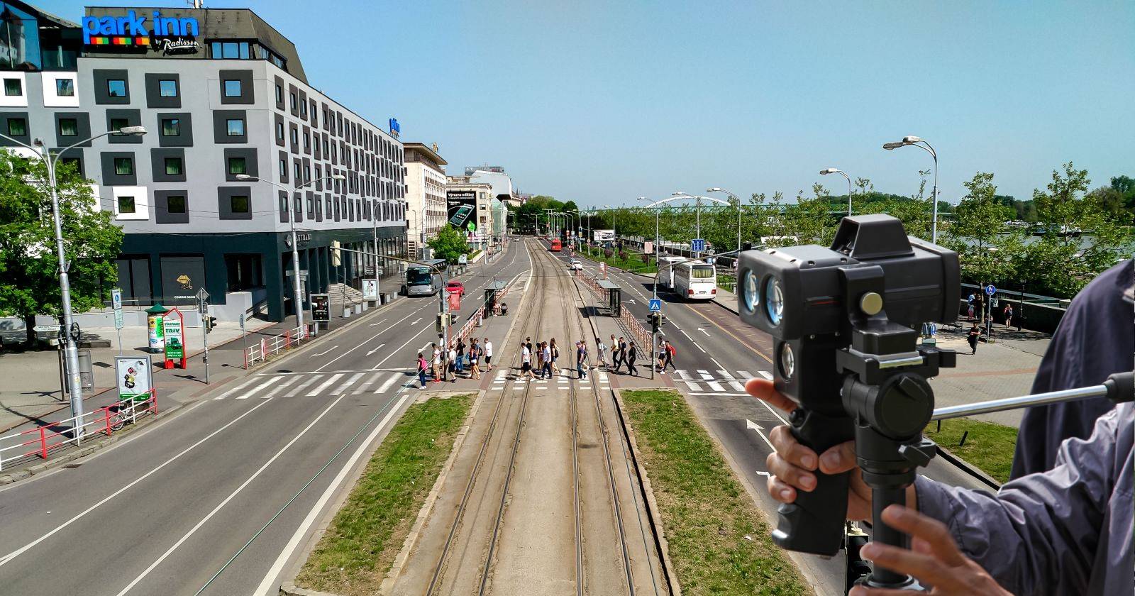 Straße in Bratislava, welche von Fußgängern überquert wird, daneben die Hände von Polizisten, welche eine Radarpistole halten