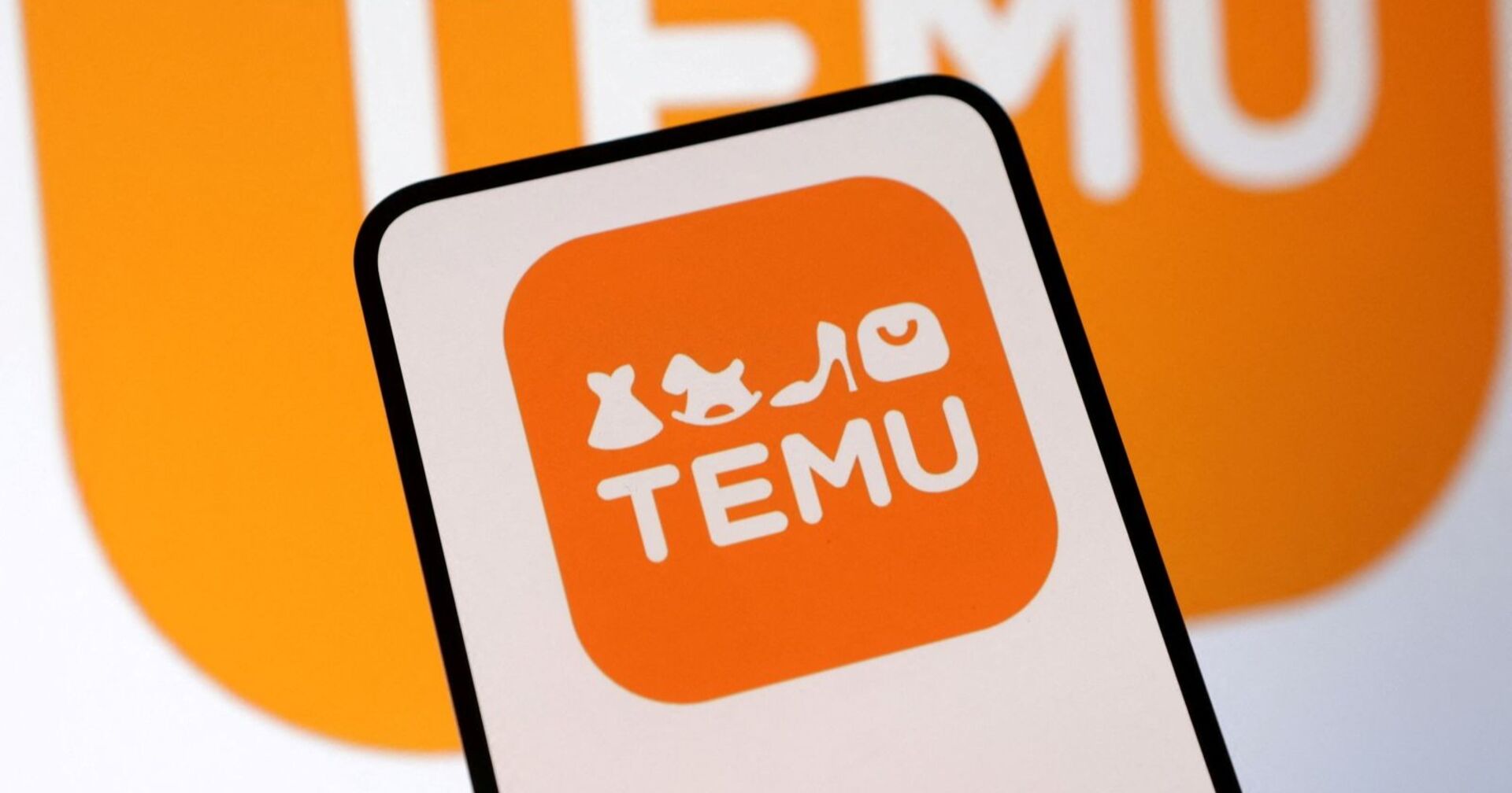 Smartphone mit dem orangefarbenen Temu-Logo, im Hintergrund unscharf ein vergrößerter Schriftzug der Plattform.