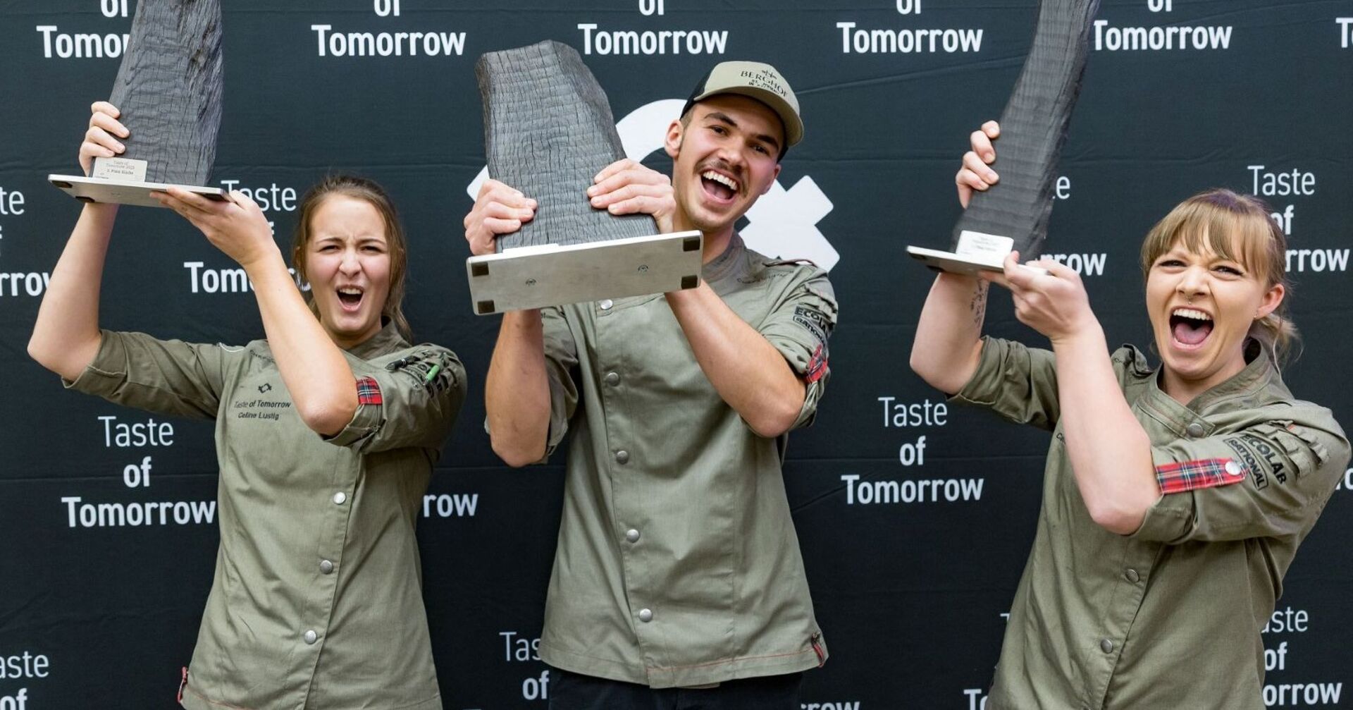 Die drei Gewinner heben ihre Pokale in die Höhe.