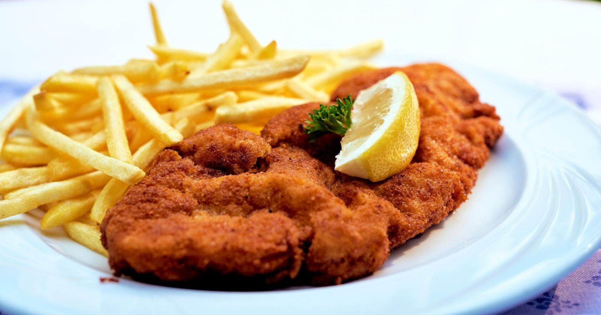 Teller mit Wiener Schnitzel, Zitronenspalte und Pommes frites, traditionelles österreichisches Gericht wie es auch  im Thomawirt serviert wird.