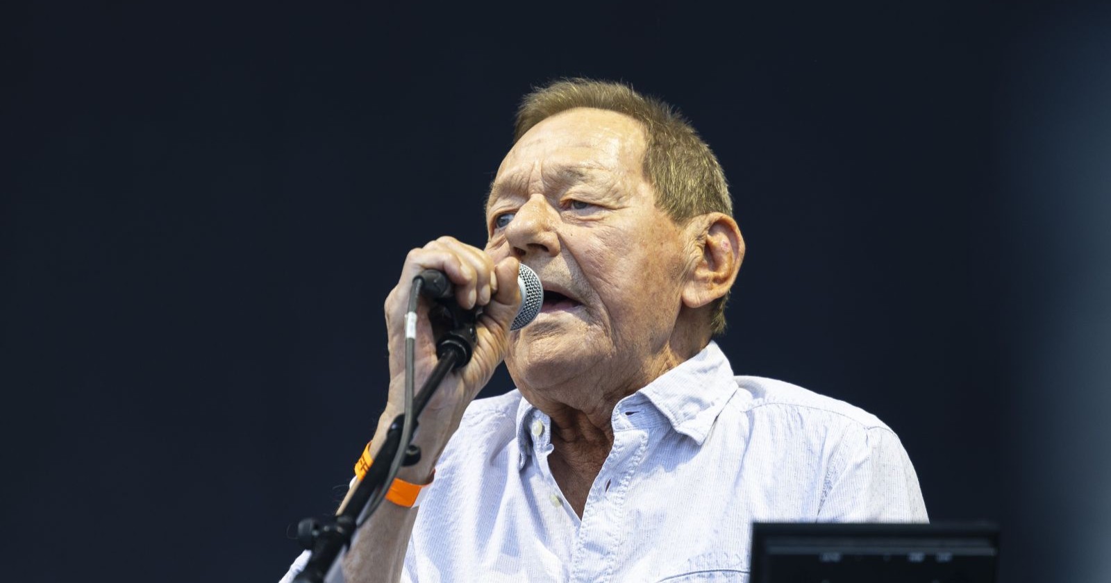 Wolfgang Ambros singt bei einem Auftritt in ein Mikrofon, das er in einer Hand nahe am Mund hält.