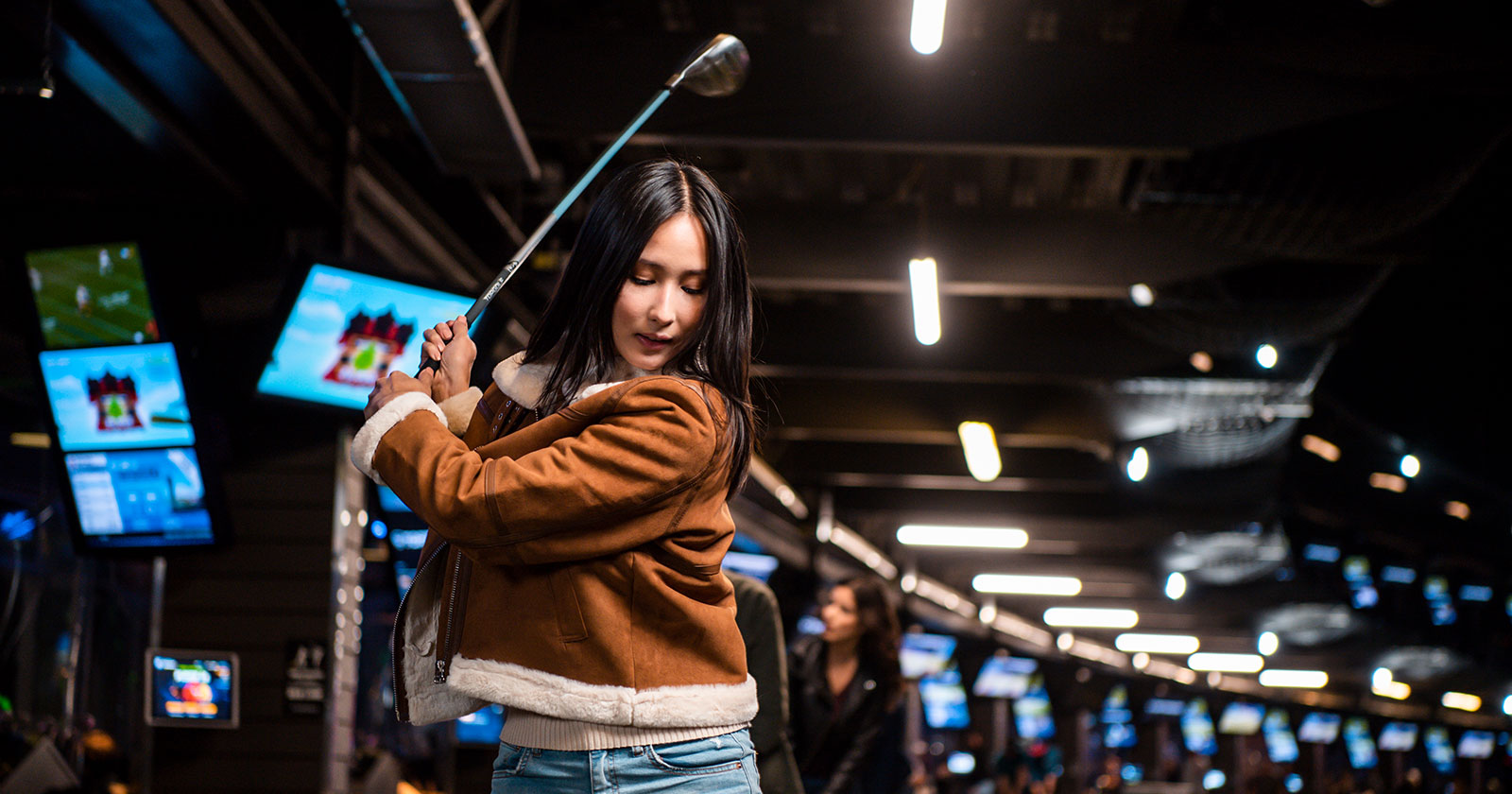 Junge Frau beim Abschlag in einer überdachten Golf-Anlage | Credit: Topgolf Wien