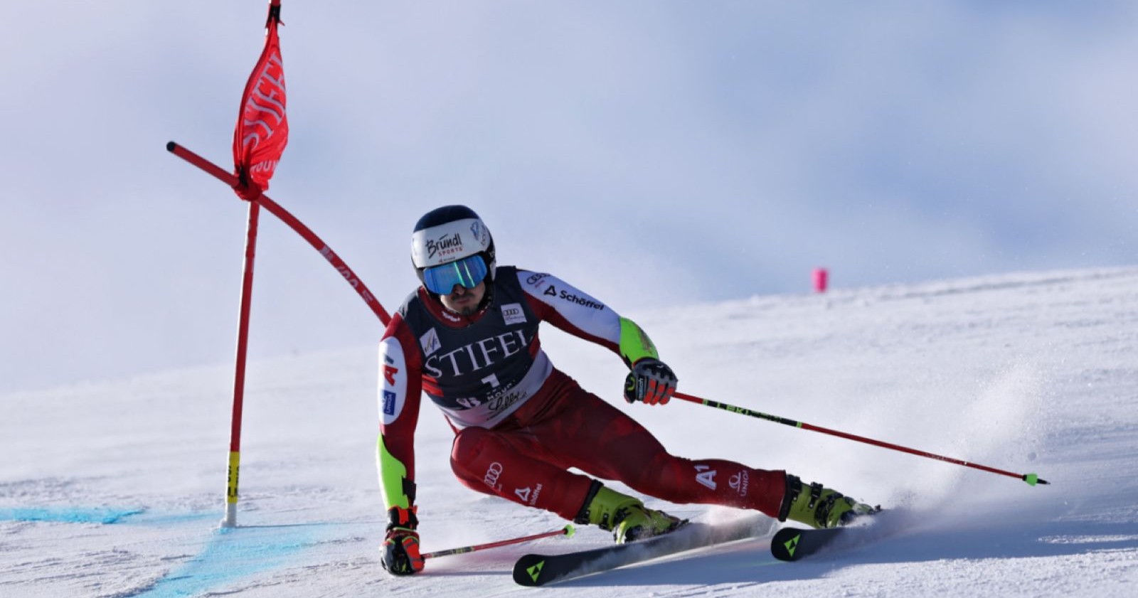 Stefan Brennsteiner nimmt eine enge Riesentorlauf-Kurve im Schnee, während er mit hoher Geschwindigkeit an einem Tor vorbeifährt.