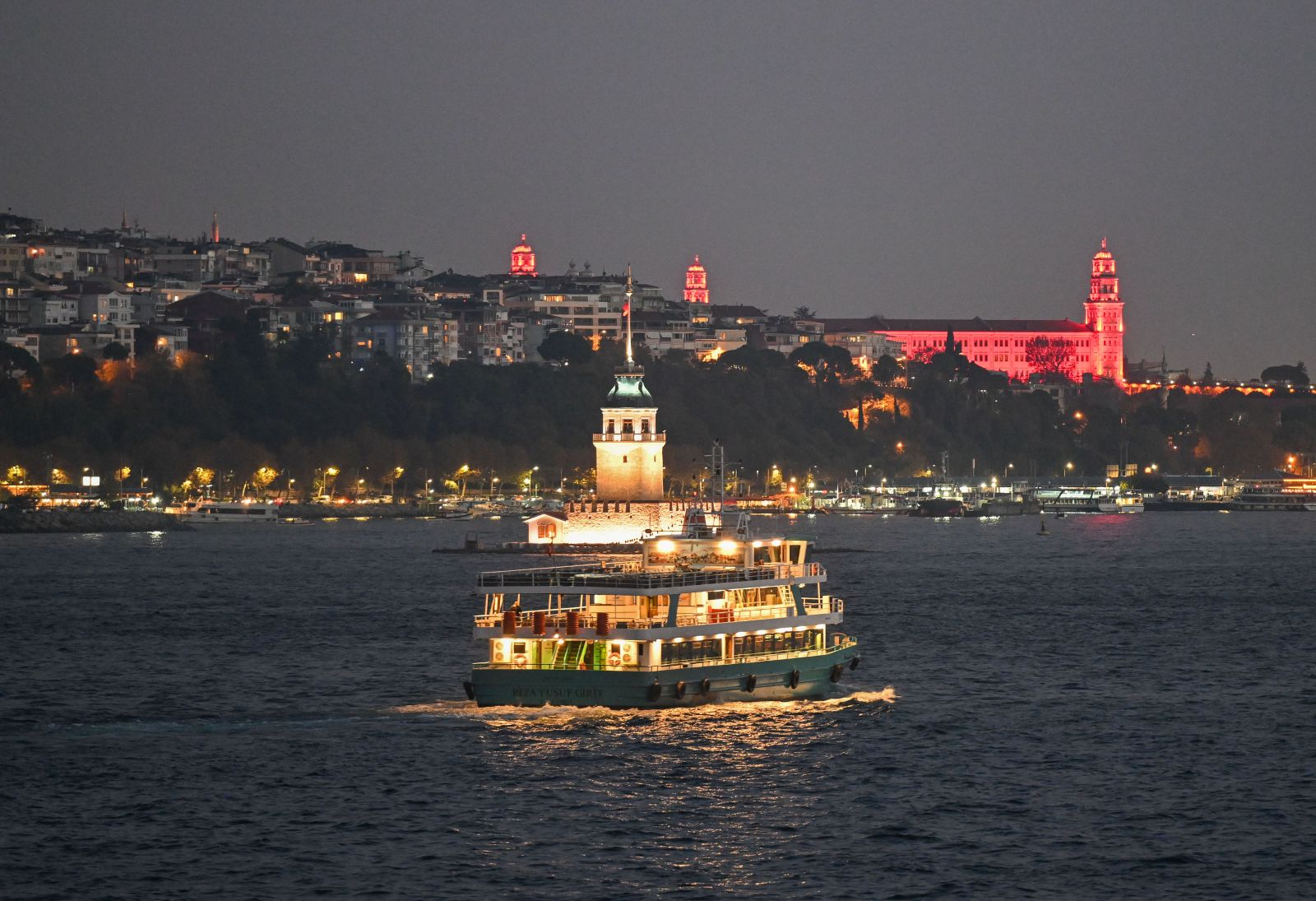 Beleuchtetes Schiff vor einer Stadt im Abendlicht