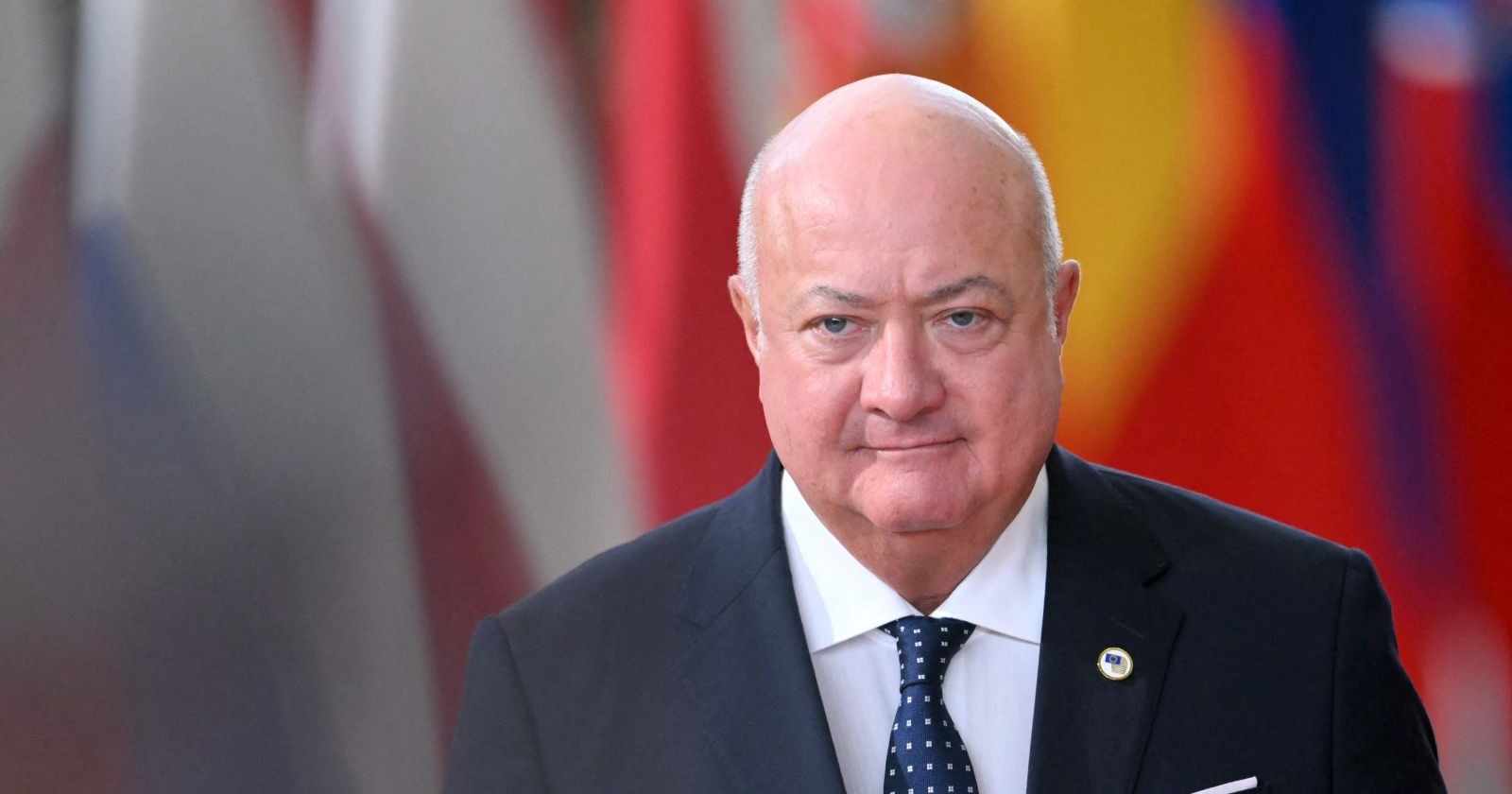 Christian Stocker, österreichischer Bundeskanzler, blickt in die Kamera; im Hintergrund sind unscharf Landesflaggen zu sehen.