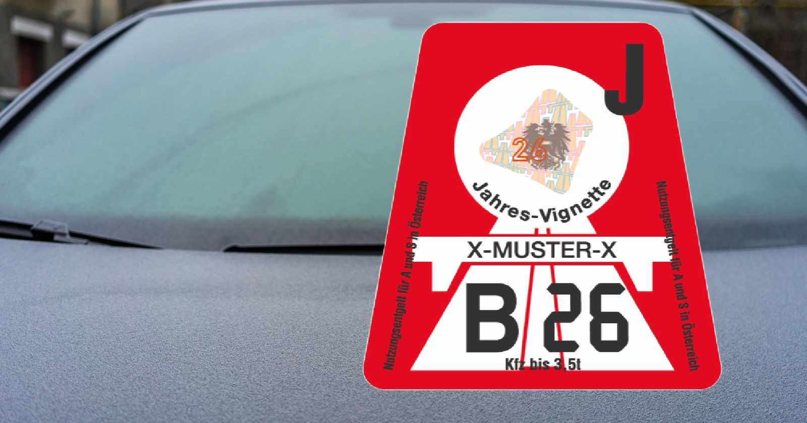 Rote österreichische Jahresvignette 2026 mit der Aufschrift „Jahres-Vignette“ und Kennzeichenfeld, angebracht an einer Autoscheibe.
