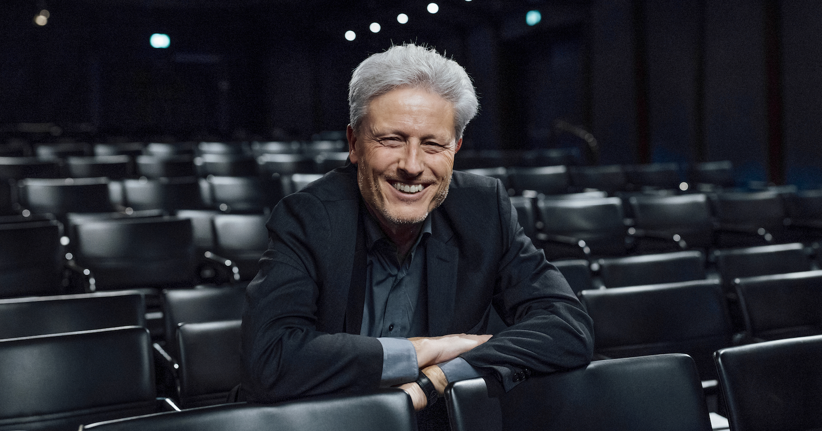 Florian Scheuba in dunklem Hemd und schwarzen Anzug im Zuschauerraum eines Theaters