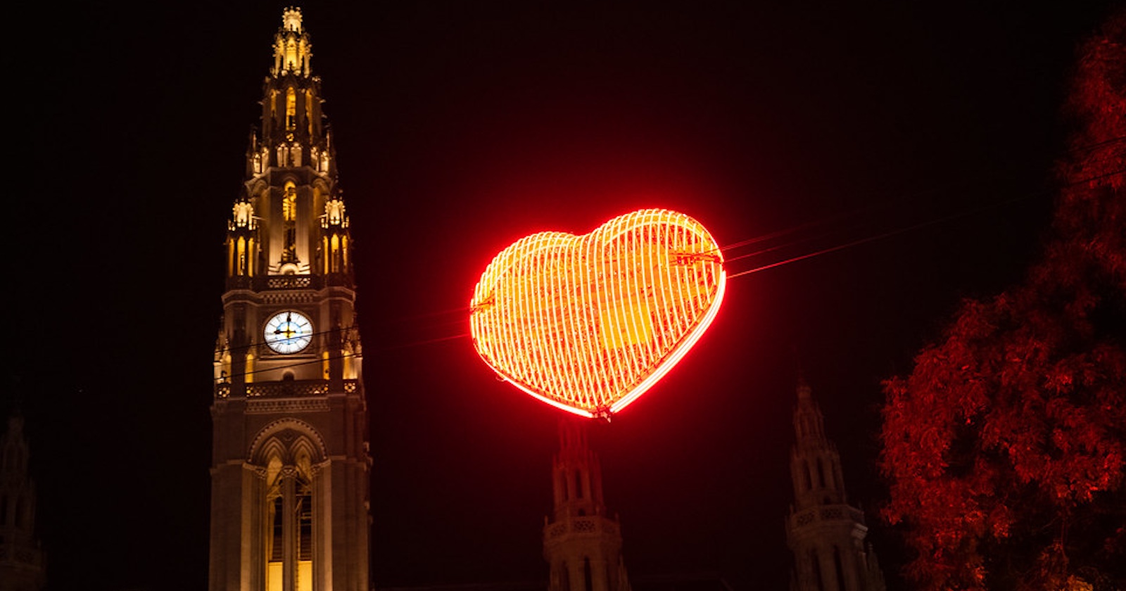 illuminiertes, rot leuchtes Herz auf Fäden vor dem festlich beleuchteten Wiener Rathaus