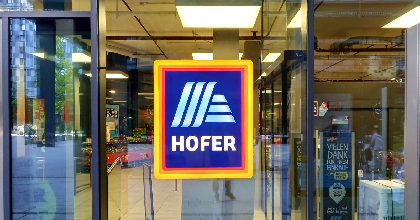 Eingang einer HOFER-Filiale mit gut sichtbarem HOFER-Logo an der Glasfront, der Discount hat einen Rückruf für Forellen-Filets gestartet