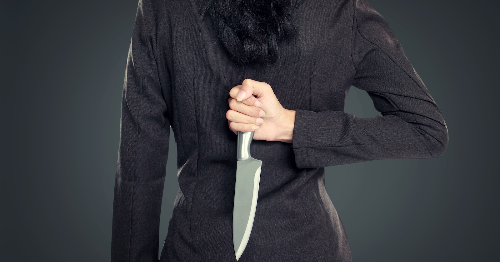 Frau in Kostümjacke von hinten mit Messer in der Hand