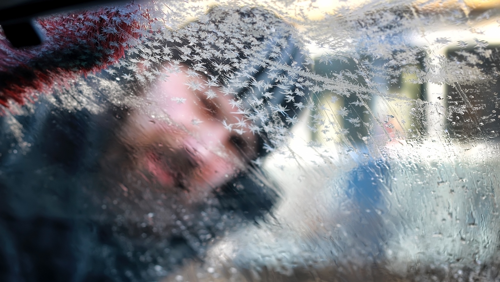 Mann schaut von außen durch vereiste Fenster in ein auto