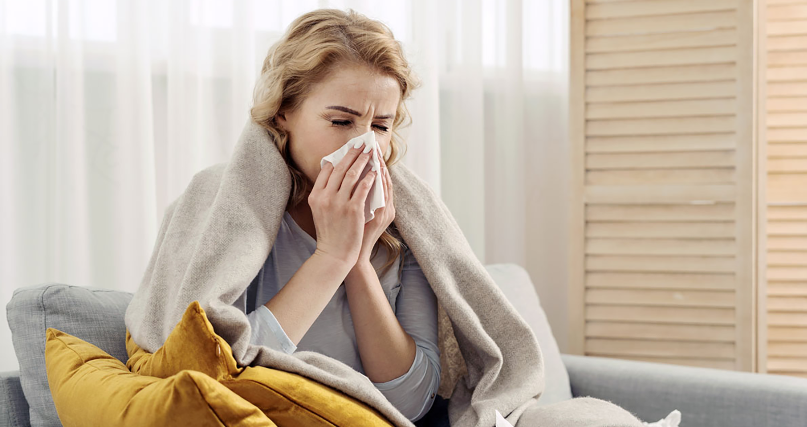 Frau sitzt mit Erkältung auf einer Couch | Credit: stock.adobe.com/brizmaker