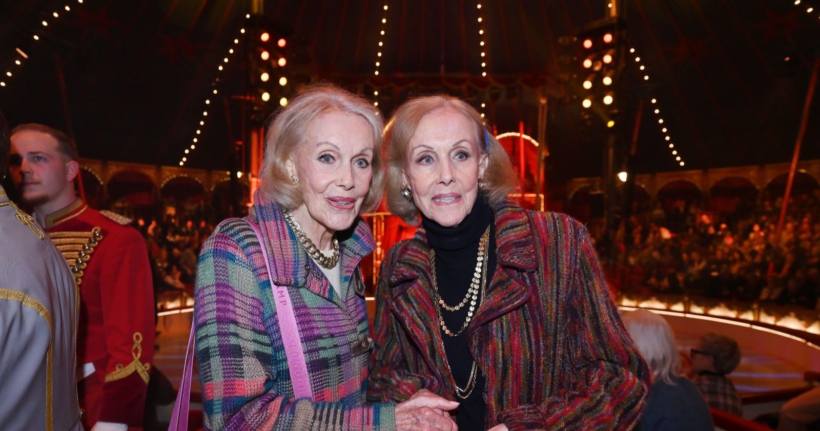 Alice und Ellen Kessler stehen eng nebeneinander im Zuschauerbereich des Circus Roncalli; die Kessler-Zwillinge lächeln in die Kamera während ihres letzten öffentlichen Auftritts.