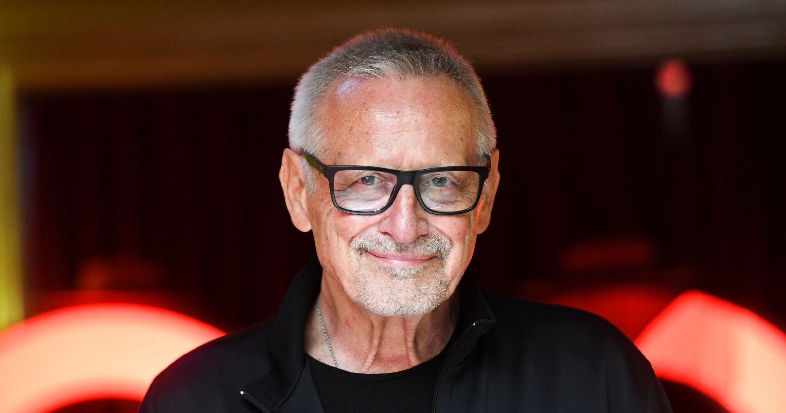 Konstantin Wecker mit Brille und kurzem grauen Haar, lächelnd vor dunklem Hintergrund, trotz schwerer Krankheit ist er dankbar.