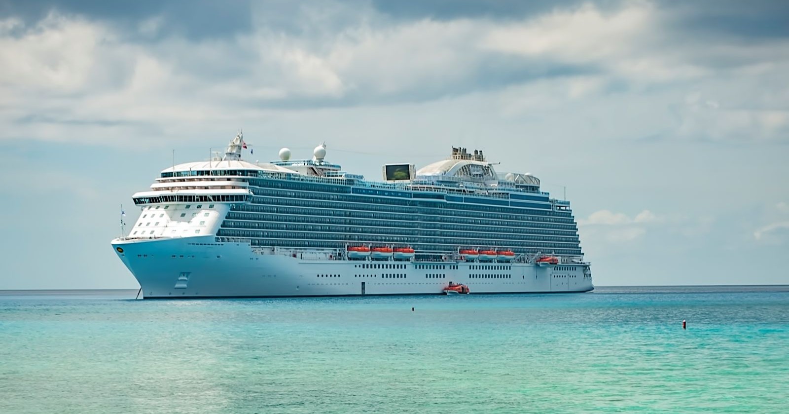 Großes Kreuzfahrtschiff auf türkisblauem Meer unter bewölktem Himmel, Symbolbild für den Fall der auf See verstorbenen 18-jährigen Passagierin.