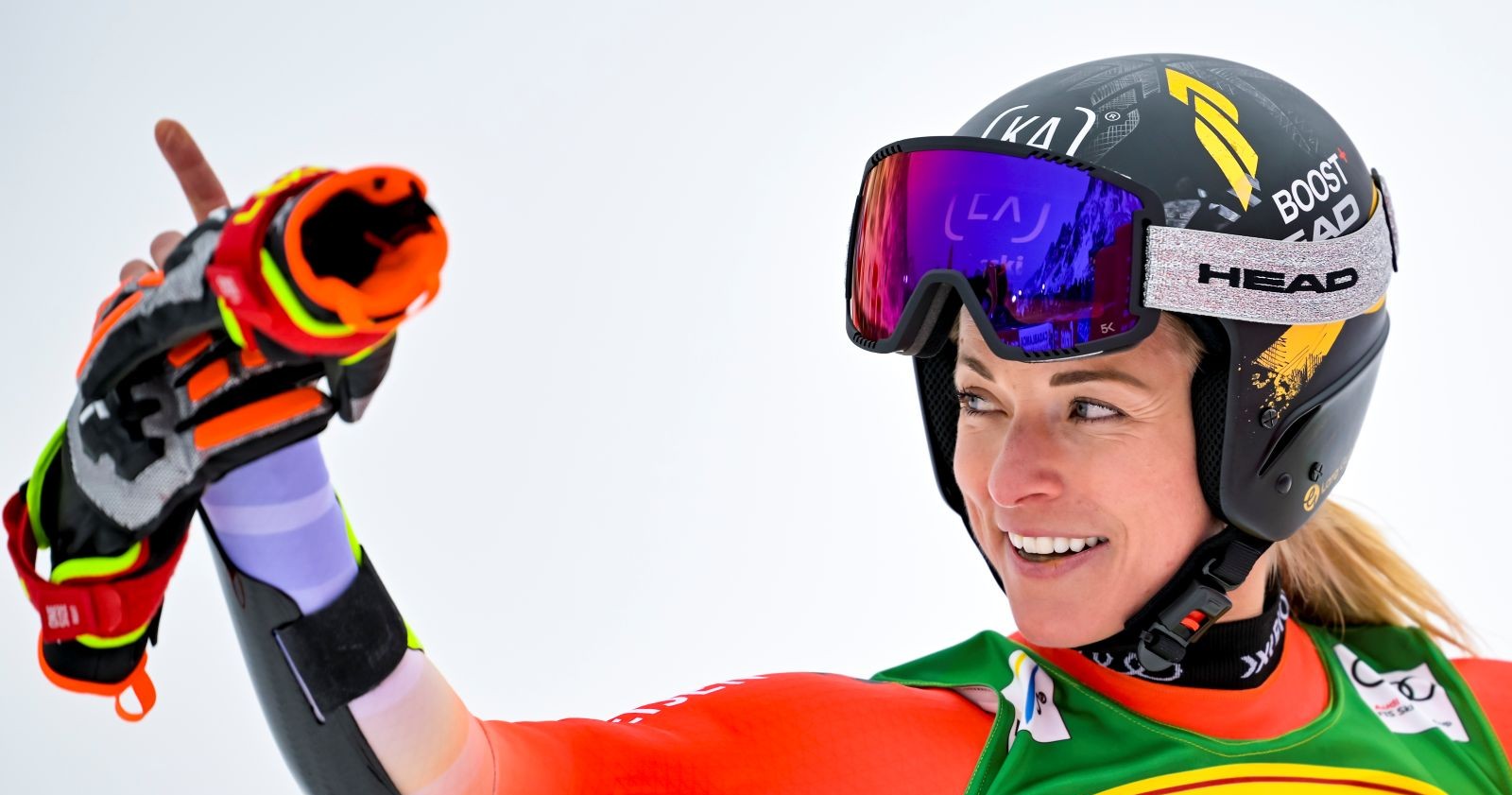 Lara Gut-Behrami mit Helm und Skibrille auf der Piste, im Rennanzug und mit Skihandschuhen, lächelnd und konzentriert.