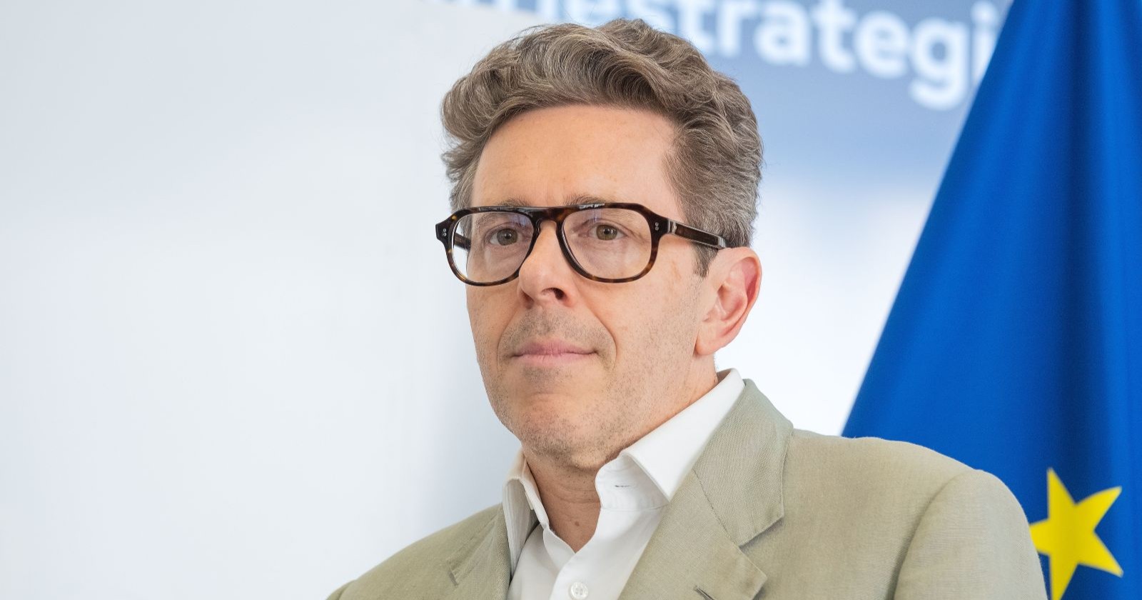 Harald Mahrer vor seinem Rücktritt bei einer Presseveranstaltung vor neutralem Hintergrund und EU-Flagge.