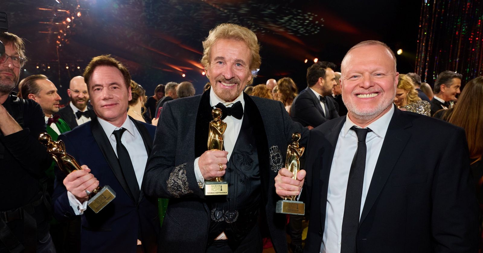 Thomas Gottschalk hält bei der Kurier Romy 2025 in Kitzbühel seine Diamant-Romy in den Händen, flankiert von den zwei weiteren Sonderpreisträgern Bully Herbig und Stefan Raab, umgeben von Gästen in festlicher Abendgarderobe.