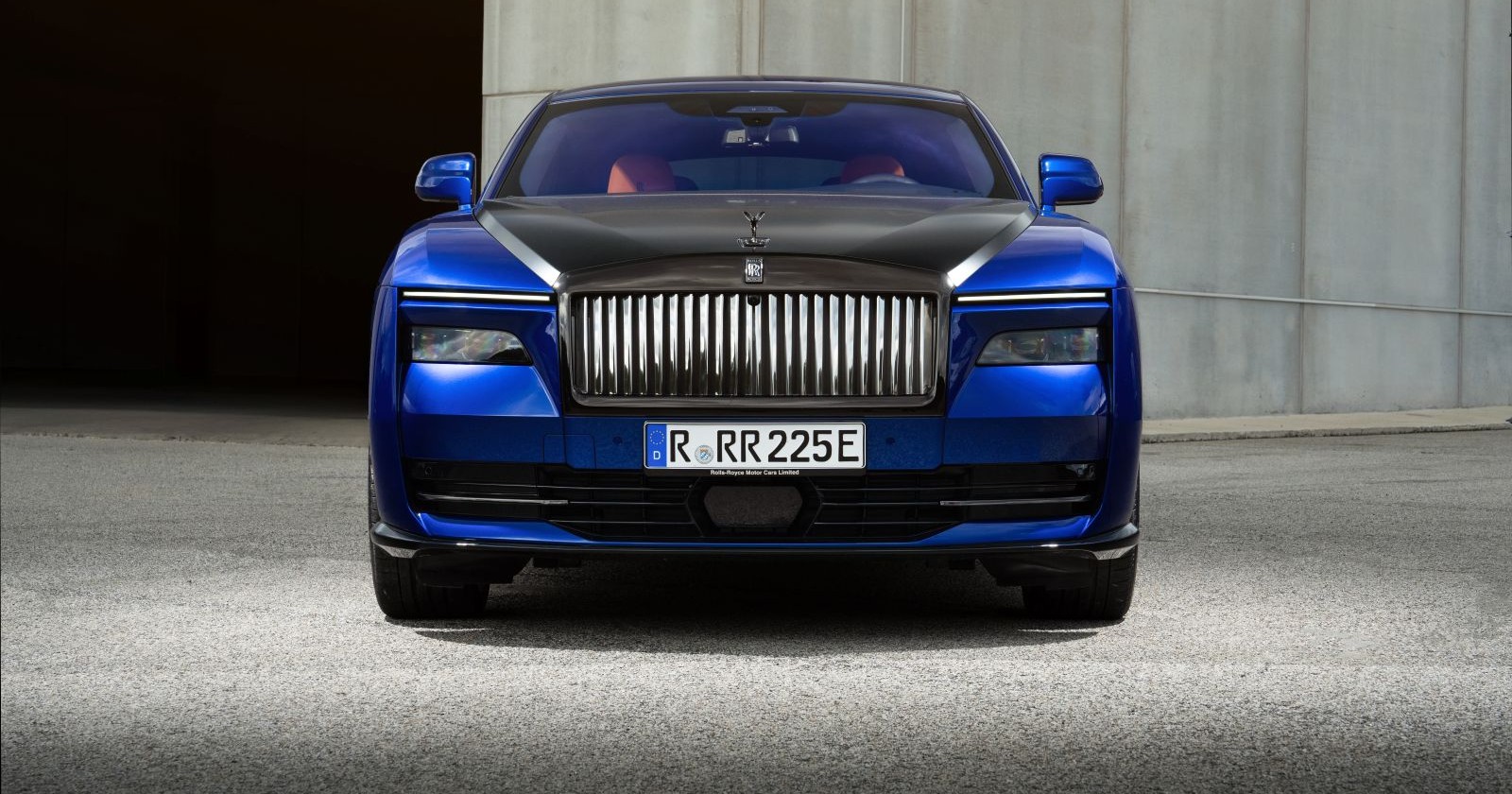 Ein Rolls-Royce  Black Badge Spectre park auf einem betonierten Platz. Der blaue Luxuswagen glänzt in der Sonne.